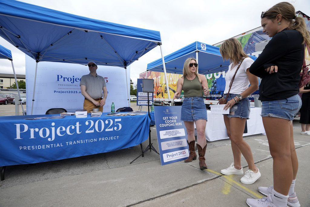 Kristen Eichamer, center, talks to fairgoers in the Project 2025 tent at the Iowa State Fair, Aug. 14, 2023, in Des Moines, Iowa. With more than a year to go before the 2024 election, a constellation of conservative organizations is preparing for a possible second White House term for Donald Trump. The Project 2025 effort is being led by the Heritage Foundation think tank. (AP Photo/Charlie Neibergall)