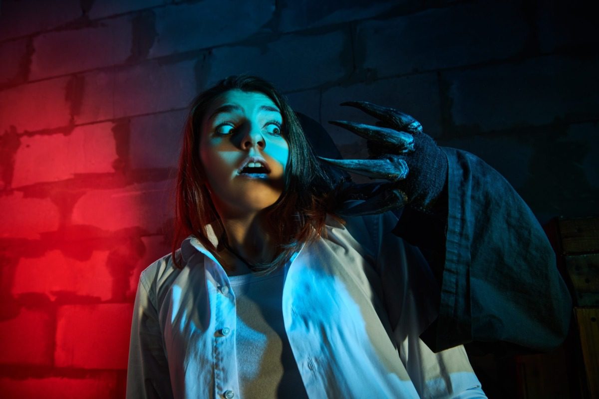 Horror film for teenagers. A frightened girl screams in horror when she stumbles upon the hand of a monster with large black claws in a dark basement. Halloween quest.